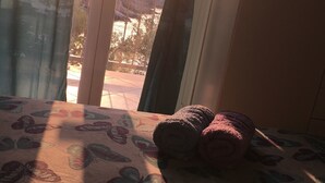 A room with a bed featuring a butterfly-patterned bedspread, a pair of rolled towels, and a view through a window with curtains. - House Kupina (Gdinj)