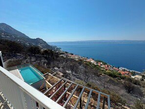 Un quartier résidentiel offrant une vue dégagée sur la mer, doté d’une piscine et bordé d’une colline à la végétation clairsemée.