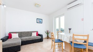 A modern living room with a grey sofa, red and white cushions, a dining table with wooden chairs, and a potted plant. - Apartments Andrea (Mandre)