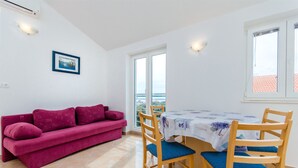 A room with a red sofa, a dining table with chairs, and a window with a view. - Apartments Andrea (Mandre)