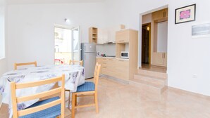 A compact kitchen with a refrigerator, microwave, and wooden cabinets. There is a dining table with chairs and a window providing natural light. - Apartments Andrea (Mandre)