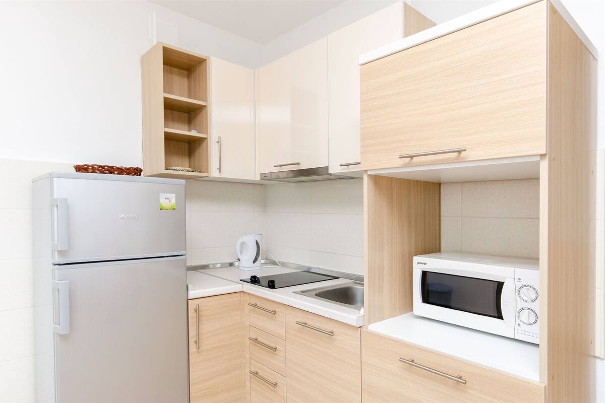 A modern kitchen with a refrigerator, microwave, kettle, and a sink.