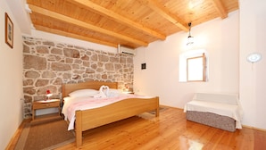 A bedroom with a wooden bed, stone wall, wooden ceiling beams, and a small bedside table with a lamp. - House Paklenica Stone Beauty (Starigrad - Paklenica)