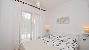 A bedroom with a bed, a window with sheer curtains, a wall-mounted light, and a small shelf with a decorative item. - Apartment Mediteraneo (Fazana)