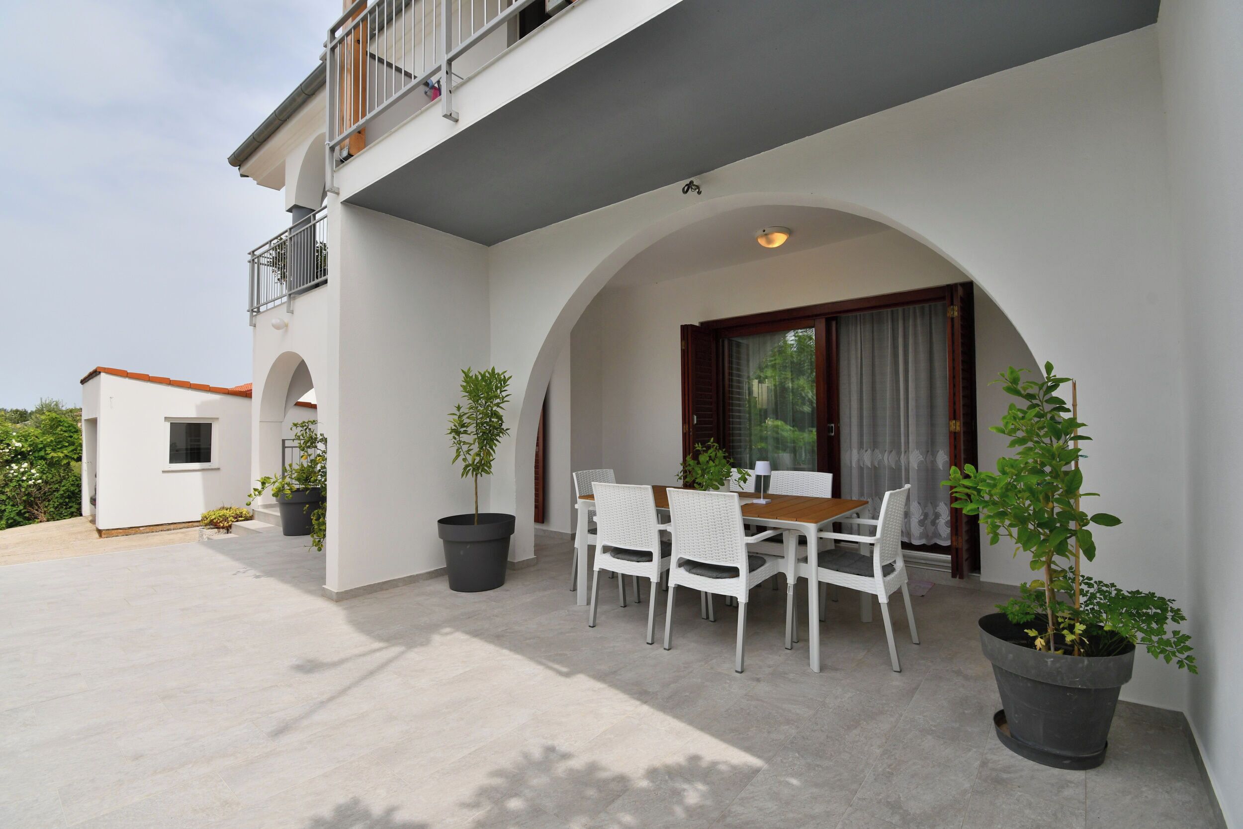 Une terrasse extérieure moderne, dotée d’une table et de chaises, et agrémentée de plantes en pot.