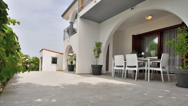A patio area with a table and chairs, potted plants, and a building with a balcony. - Apartment Mediteraneo (Fazana)