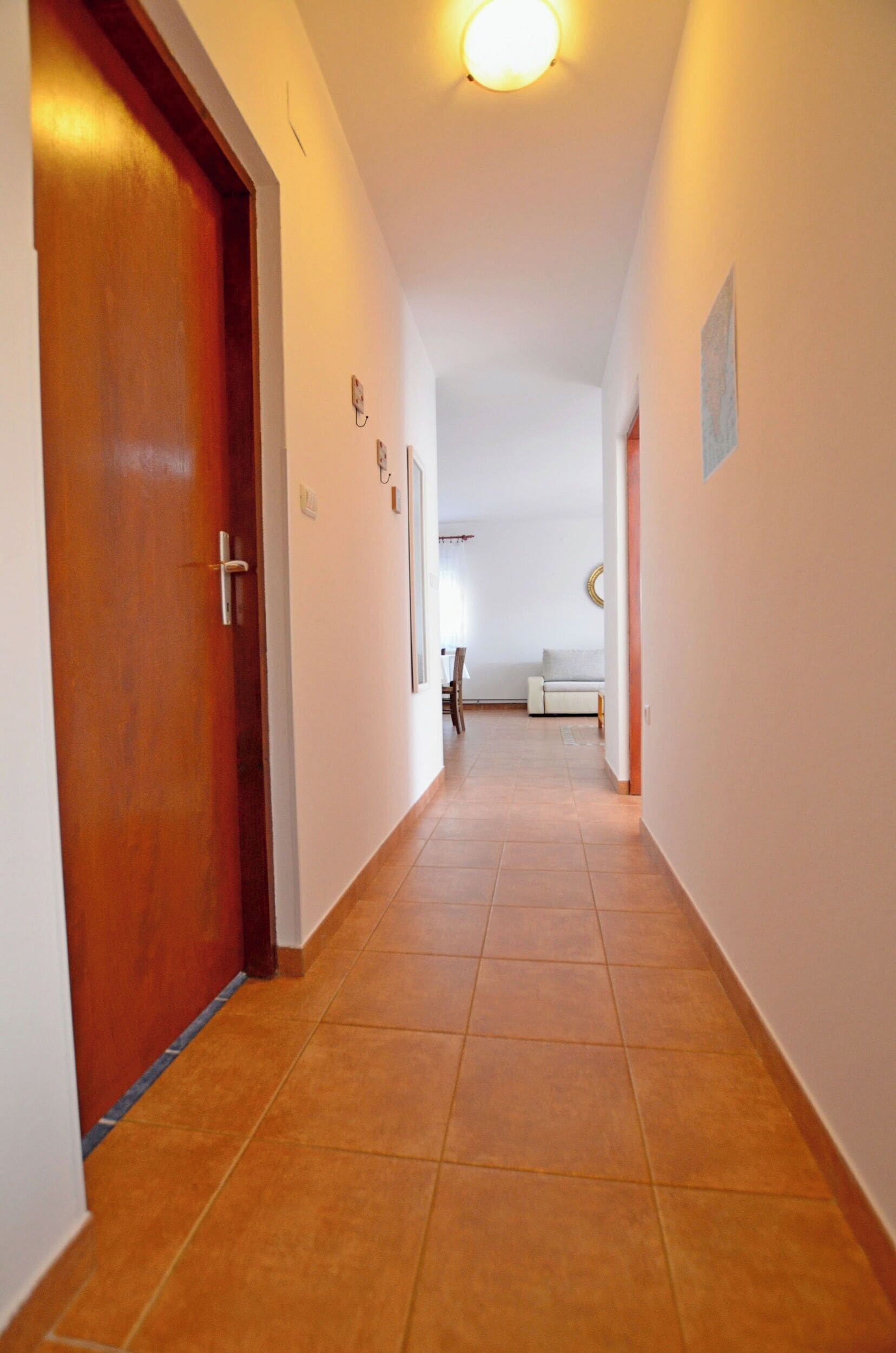 Un couloir avec une porte en bois, un sol carrelé et un luminaire au plafond.