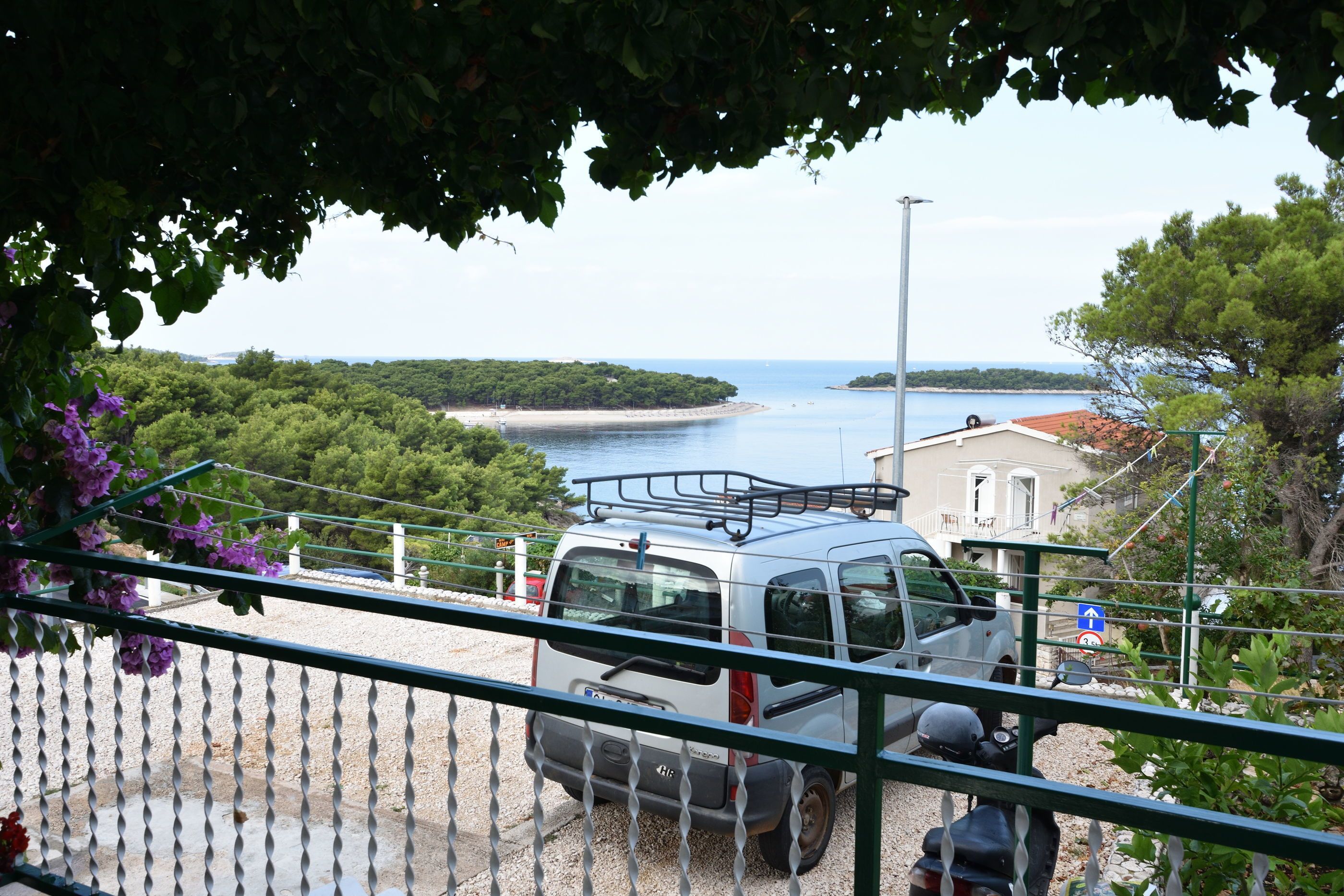 A white van parked on a gravel area with a view of a coastal landscape, including a beach and a body of water.