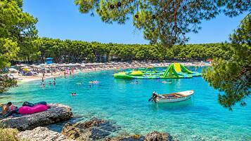 Ein Strand mit klarem türkisblauem Wasser, aufblasbaren Wasserspielzeugen und einem Boot.