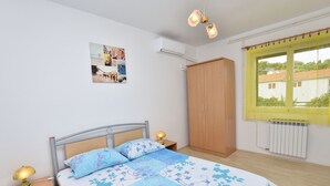 Un dormitorio con cama, armario, mesita de noche y ventana con cortina amarilla.