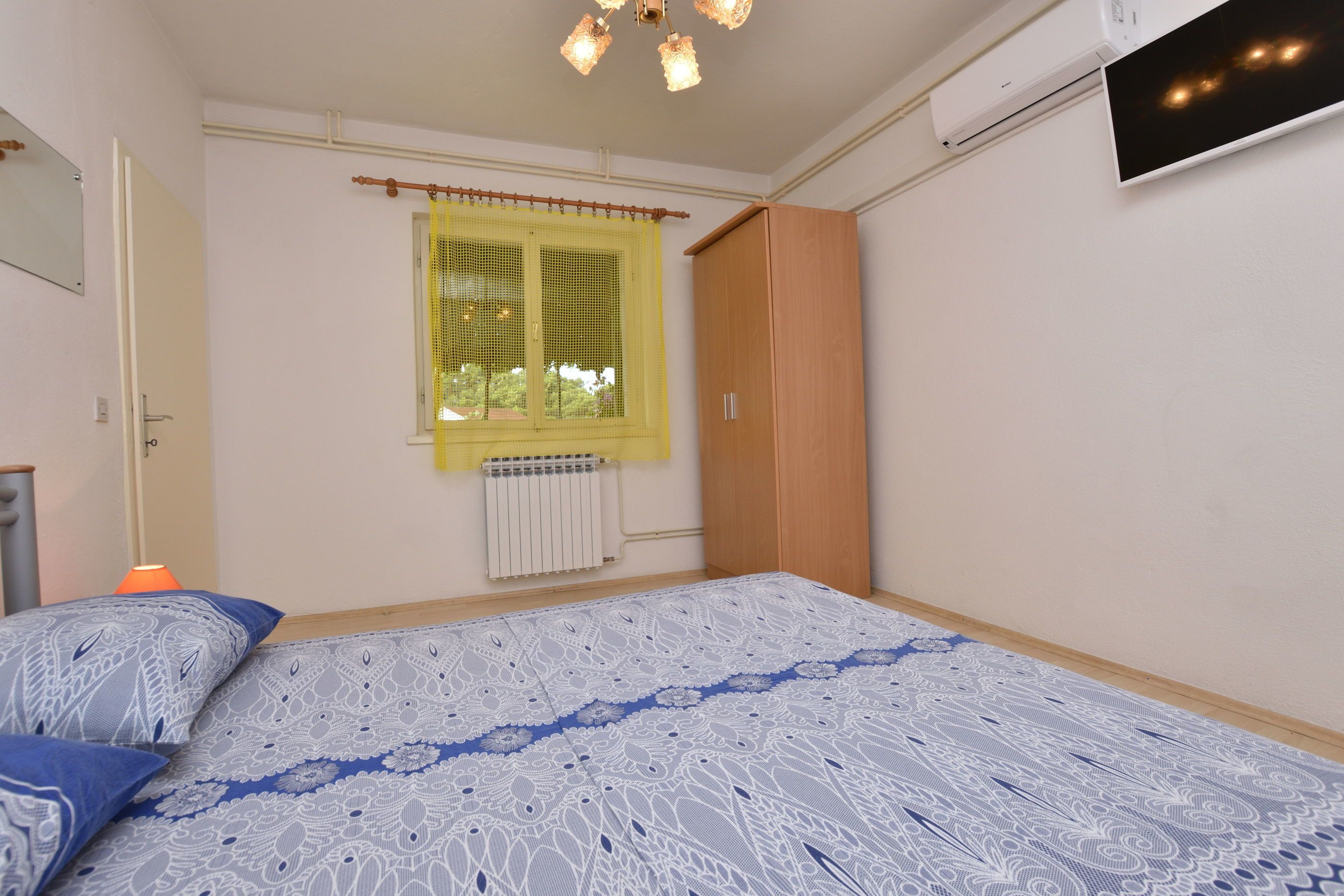 A bedroom with a bed, a window with yellow curtains, a radiator, and a wardrobe.