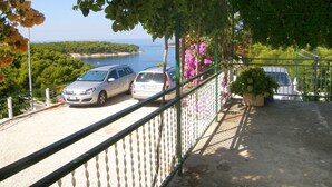 Un balcón con vista al mar y coches aparcados.