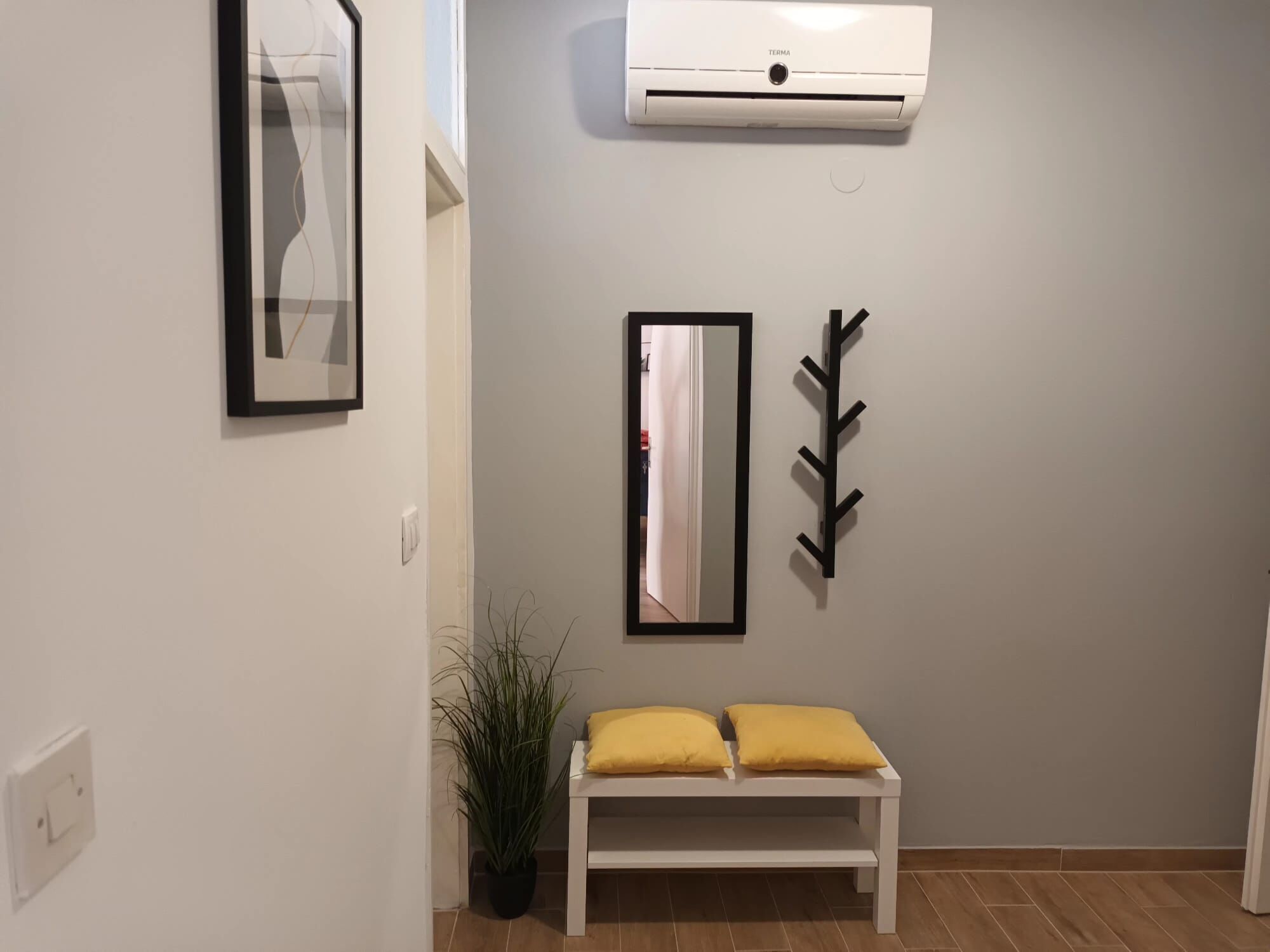 A hallway with a white bench, a potted plant, a mirror, and a wall-mounted air conditioner.