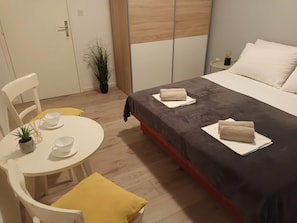 Et hotelværelse med seng, et lille bord med en plante, en stol og et natbord med lampe.