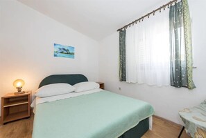 A bedroom with a bed, a nightstand with a lamp, a window with curtains, and a picture on the wall.