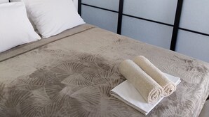 Ein ordentlich bezogenes Bett mit einer gemusterten Tagesdecke, einem zusammengerollten Handtuch und zwei Kissen.