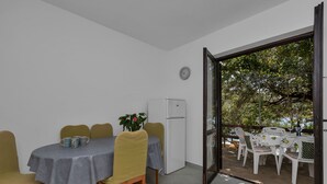 A dining area with a table set for four, a refrigerator, and a view of an outdoor patio with chairs and a table. - House Sea Rose (Zastrazisce)