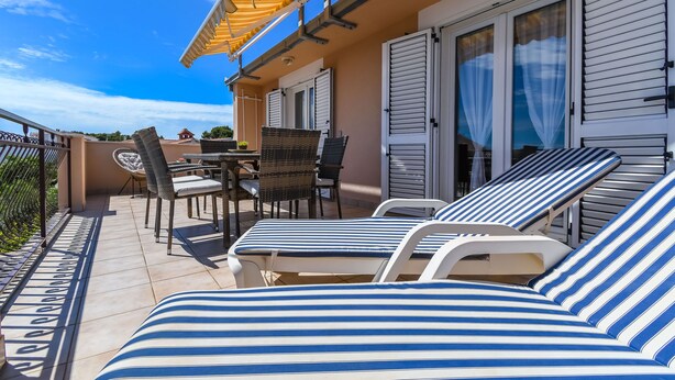 Ein Balkon mit gestreiften Liegestühlen, einem Tisch und Stühlen sowie einer Pergola darüber.