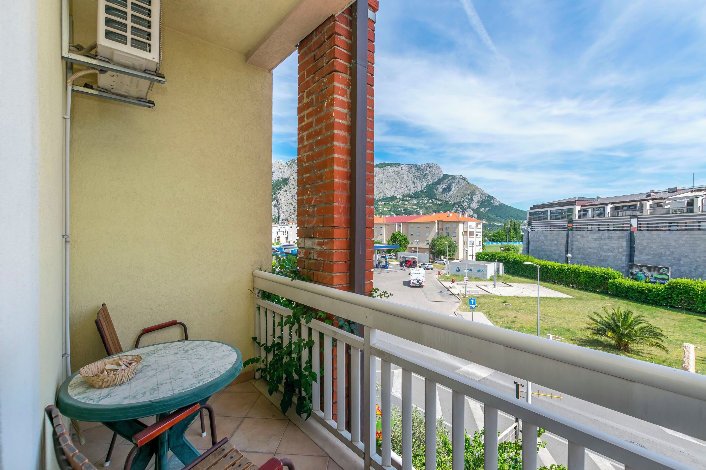 Ein Balkon mit Tisch und Stühlen, einer Ziegelstütze und Blick auf eine Straße und Berge.