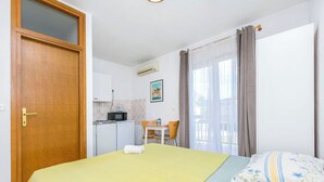 Une pièce comprenant un lit, un bureau, une chaise, un petit coin cuisine et une fenêtre avec des rideaux.