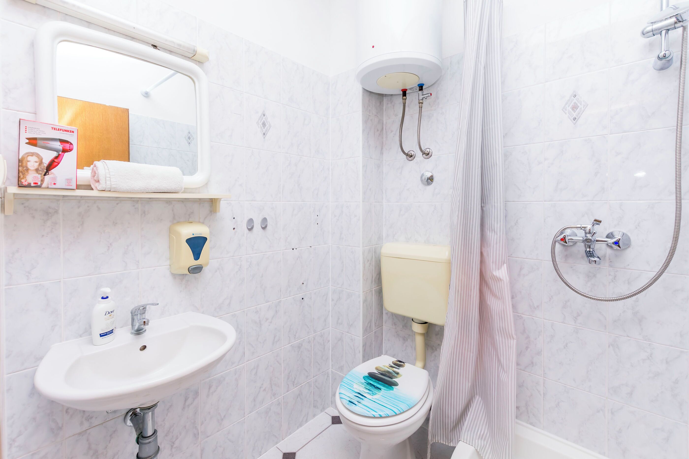A bathroom with a sink, toilet, shower, and a mirror.