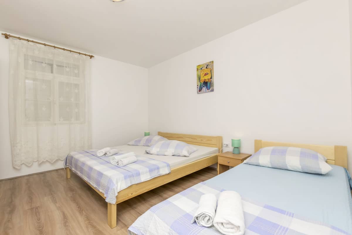 Habitació amb dos llits, una finestra amb cortina transparent, un quadre petit a la paret i un paviment de fusta.