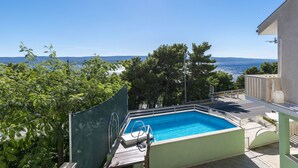 A rectangular pool with a wooden deck and a metal ladder, surrounded by trees and a clear view of the sea. - Apartments Mirko (Lokva Rogoznica)