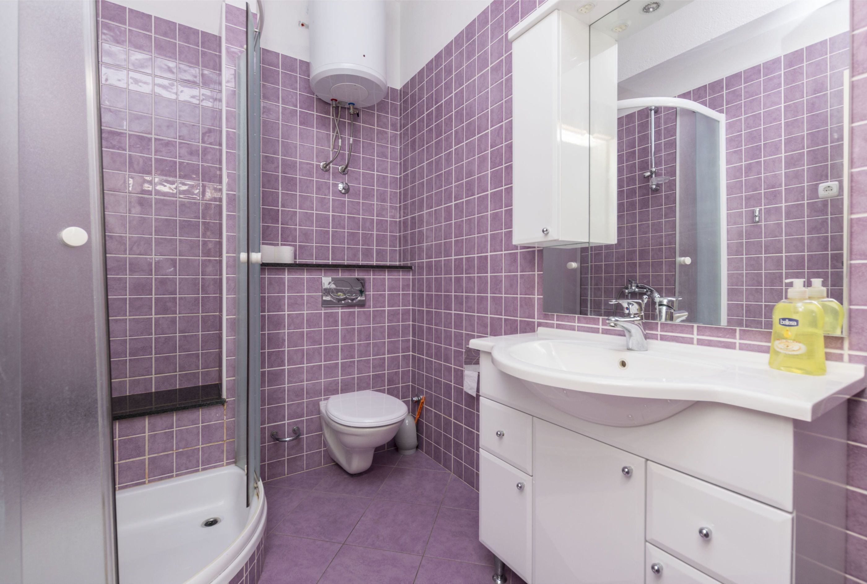 A bathroom with purple tiles, a white sink, a mirror, and a shower.