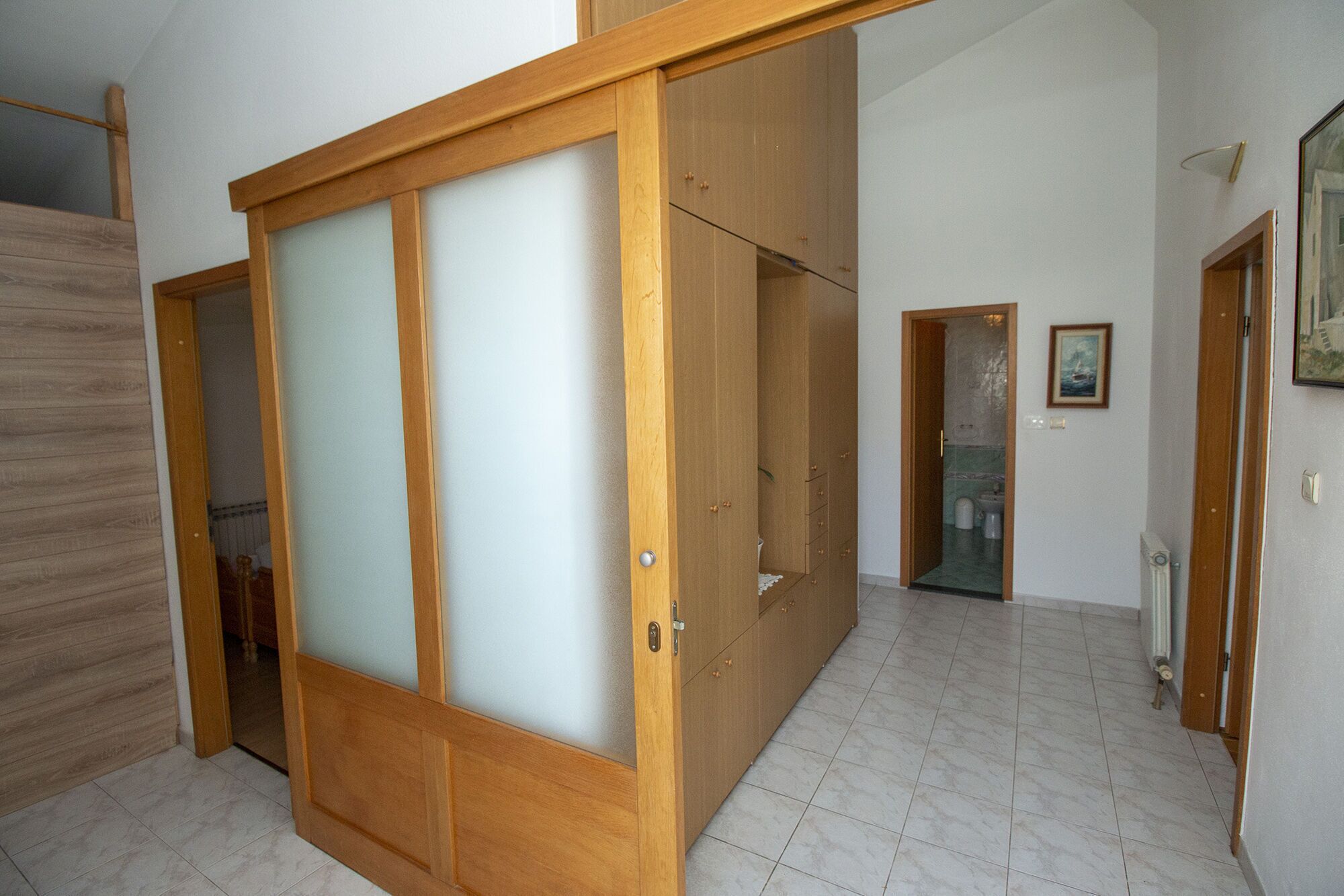 Una habitación con una puerta corredera de madera, suelo de baldosas y un baño pequeño a la vista.