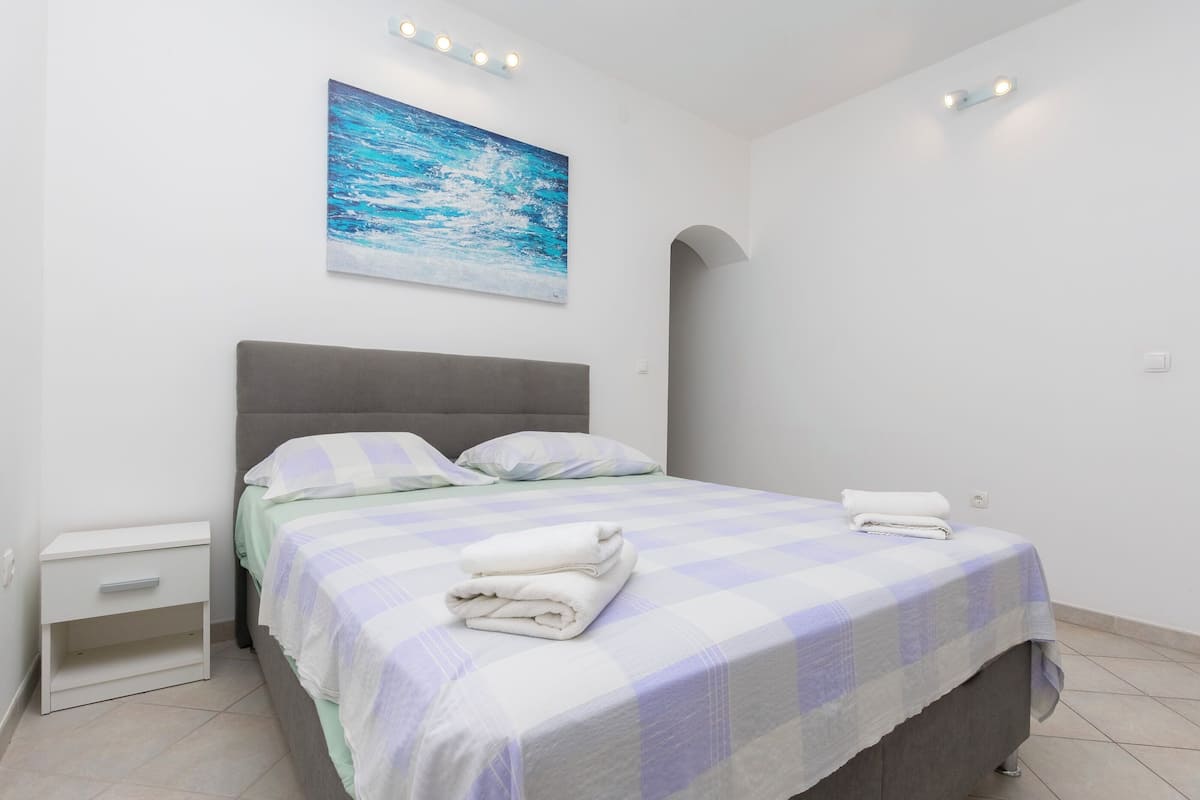 Un dormitori amb llit, una tauleta de nit, un quadre del mar i llums encastades al sostre.