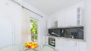 A modern kitchen with white cabinets, a black marble countertop, and a glass dining table with fruit. - Apartments Mirko (Lokva Rogoznica)