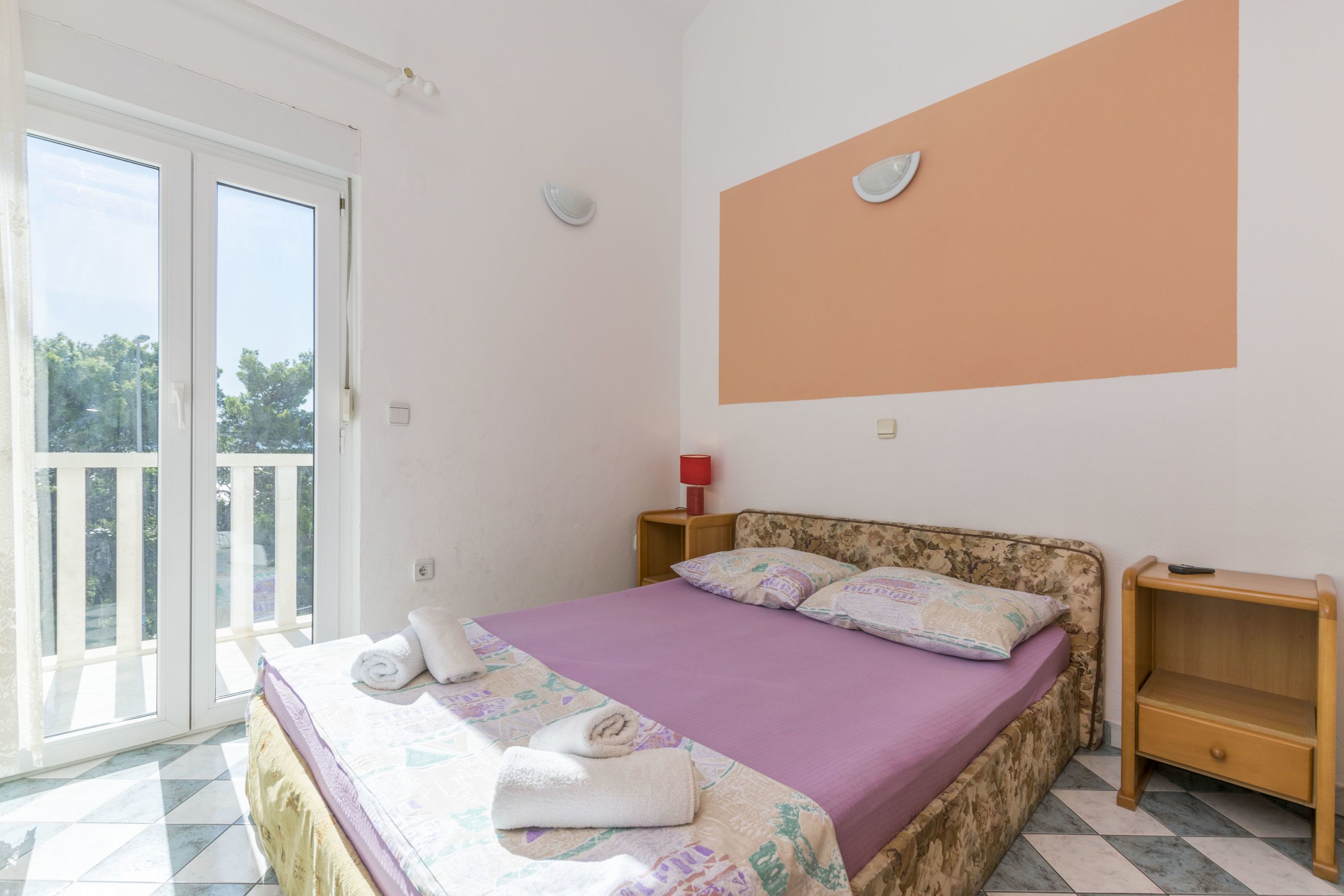 Een slaapkamer met een bed, nachtkastje, rode lamp en uitzicht op het buitenland via een schuifdeur.