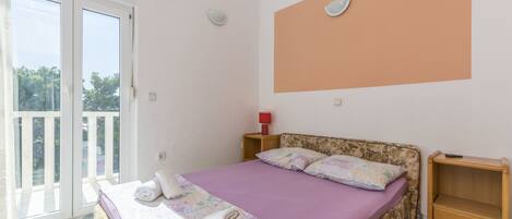 Een slaapkamer met een bed, nachtkastje, rode lamp en uitzicht op het buitenland via een schuifdeur.