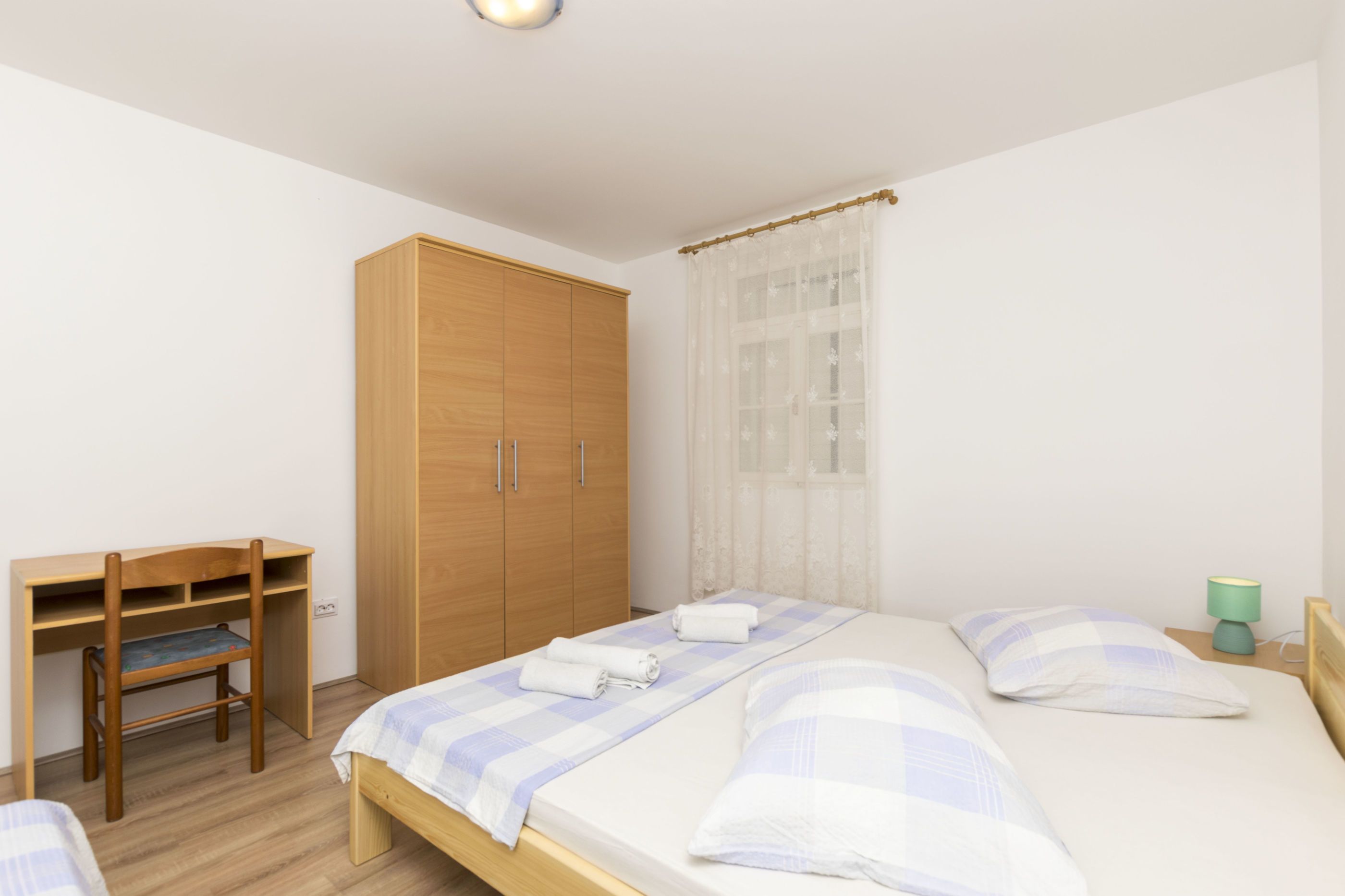 A bedroom with a wooden wardrobe, a desk, and a bed with a checkered bedspread.