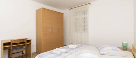A bedroom with a wooden wardrobe, a desk, and a bed with a checkered bedspread.