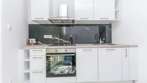 A modern kitchen with white cabinetry, a built-in oven, a stainless steel range hood, and a marble backsplash. - Apartments Mirko (Lokva Rogoznica)