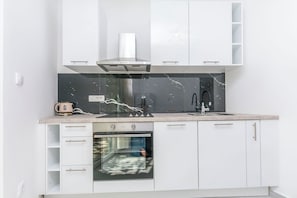 Una cocina moderna con armarios blancos, horno empotrado, campana extractora de acero inoxidable y salpicadero de mármol.