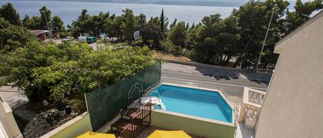A pool area with a view of the sea, surrounded by trees and yellow umbrellas.