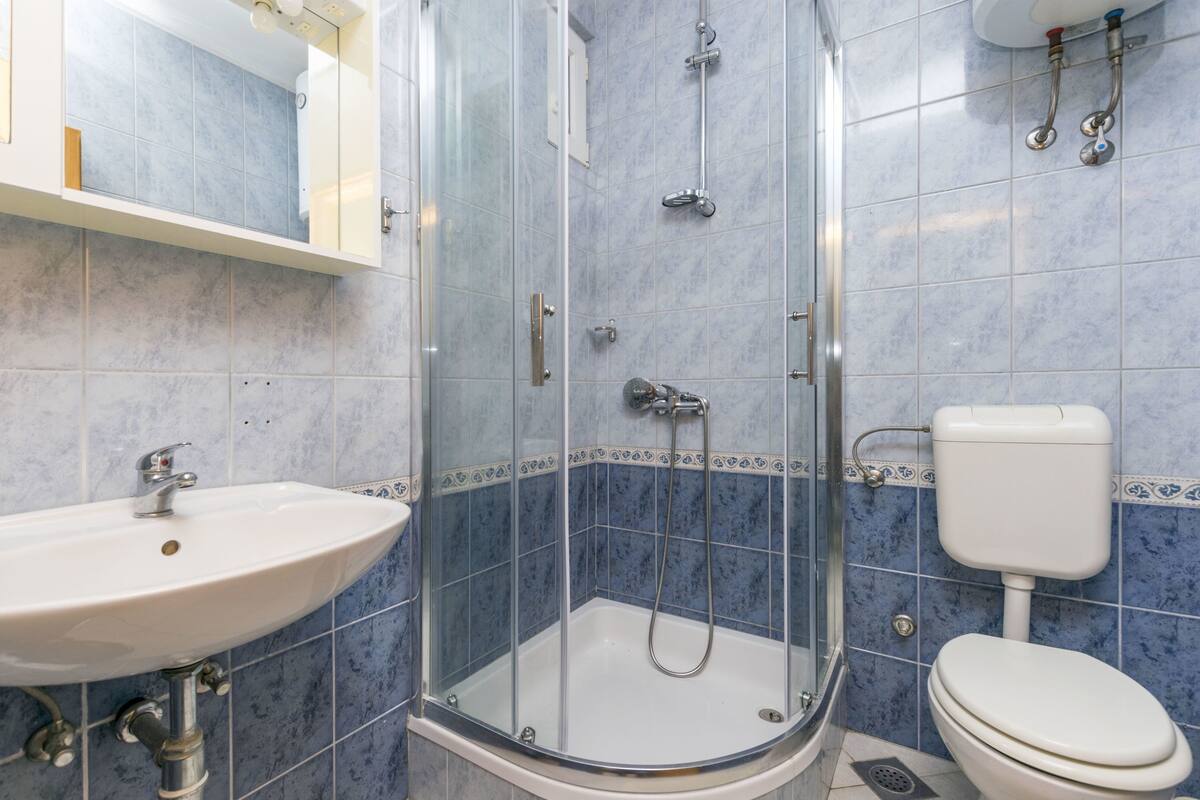 Un bany amb dutxa trencada per vidre, un lavabo blanc i un vàter.