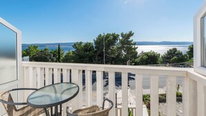 A balcony with a glass table and wicker chairs, overlooking a coastal view with trees and a clear sky. - Apartments Mirko (Lokva Rogoznica)
