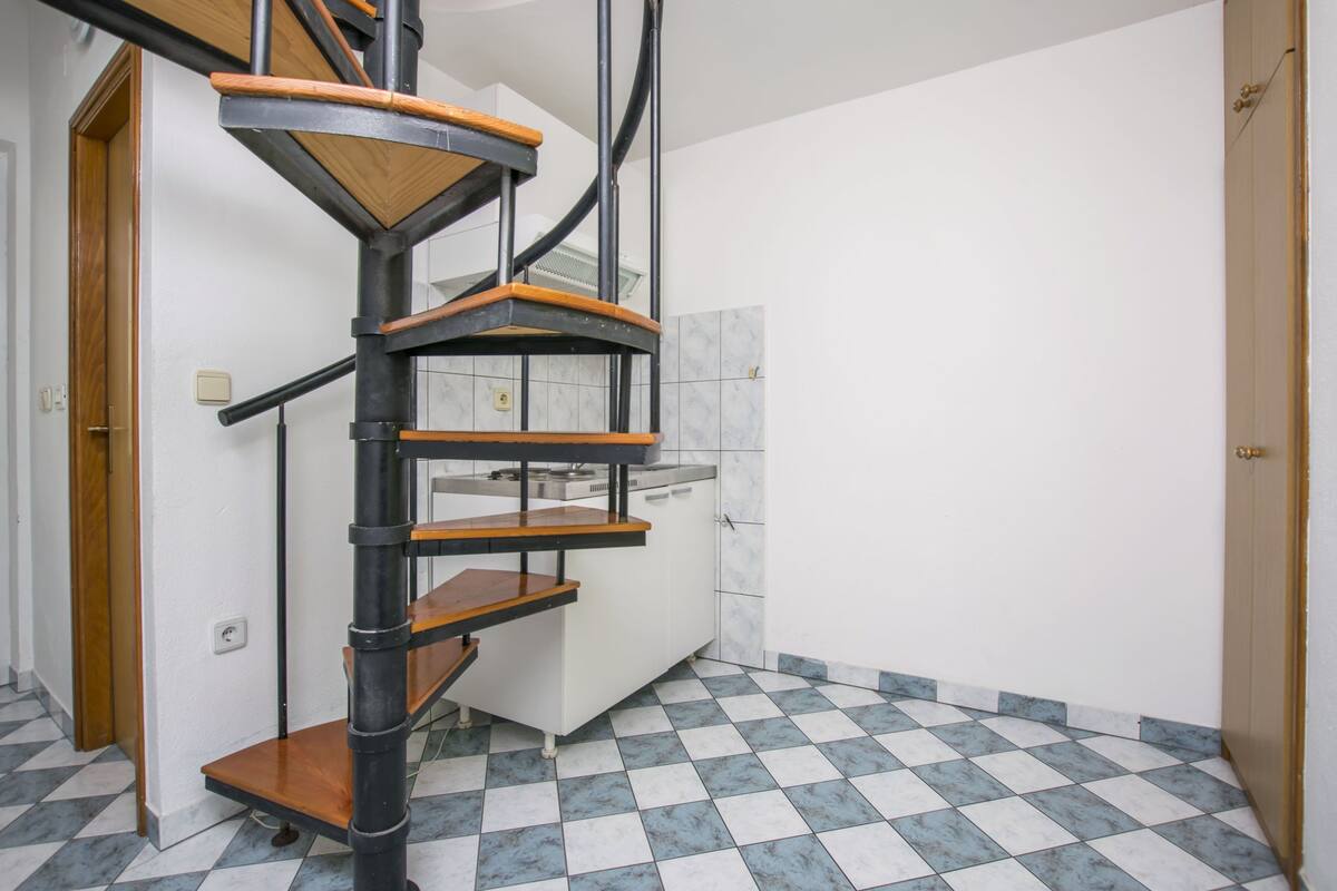 Gosairella d'espiral amb graons de fusta i baranes metàl·liques en una habitació amb terra de rajoles de pissarra.