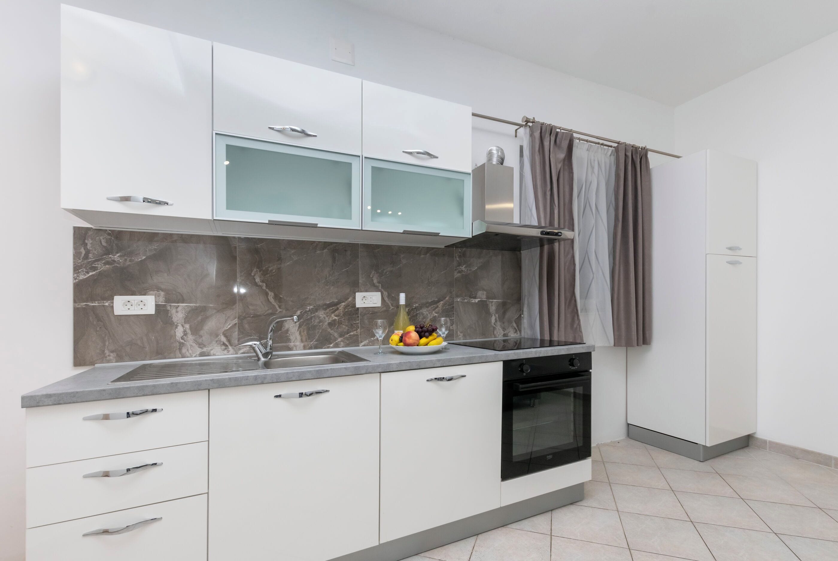 A modern kitchen with white cabinets, a marble backsplash, and a built-in oven.