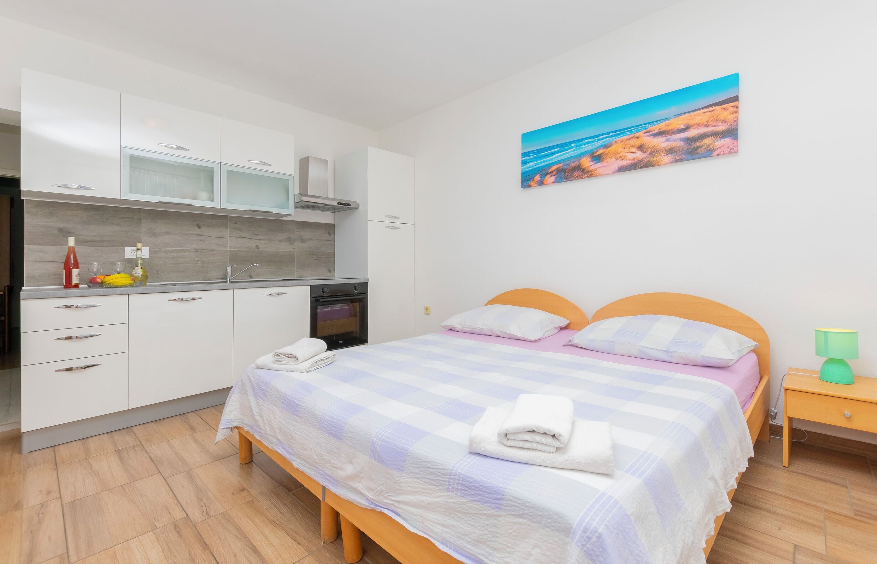 Une chambre à coucher moderne avec un lit, une table de chevet et un tableau représentant une scène de plage.