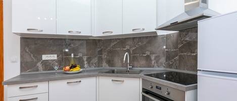 Uma cozinha moderna com armários brancos, painel de fundo de mármore, forno embutido e coifa de aço inoxidável.