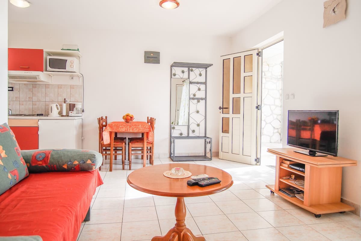 A compact living space with a kitchenette, a dining area, a sofa, a TV stand, and a small table.