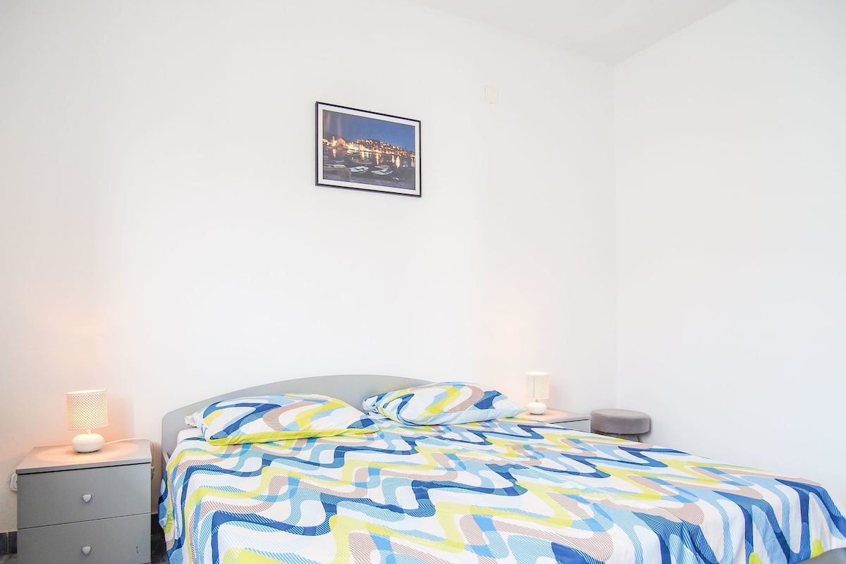 A bedroom with a bed, a nightstand, a lamp, and a framed picture on the wall.