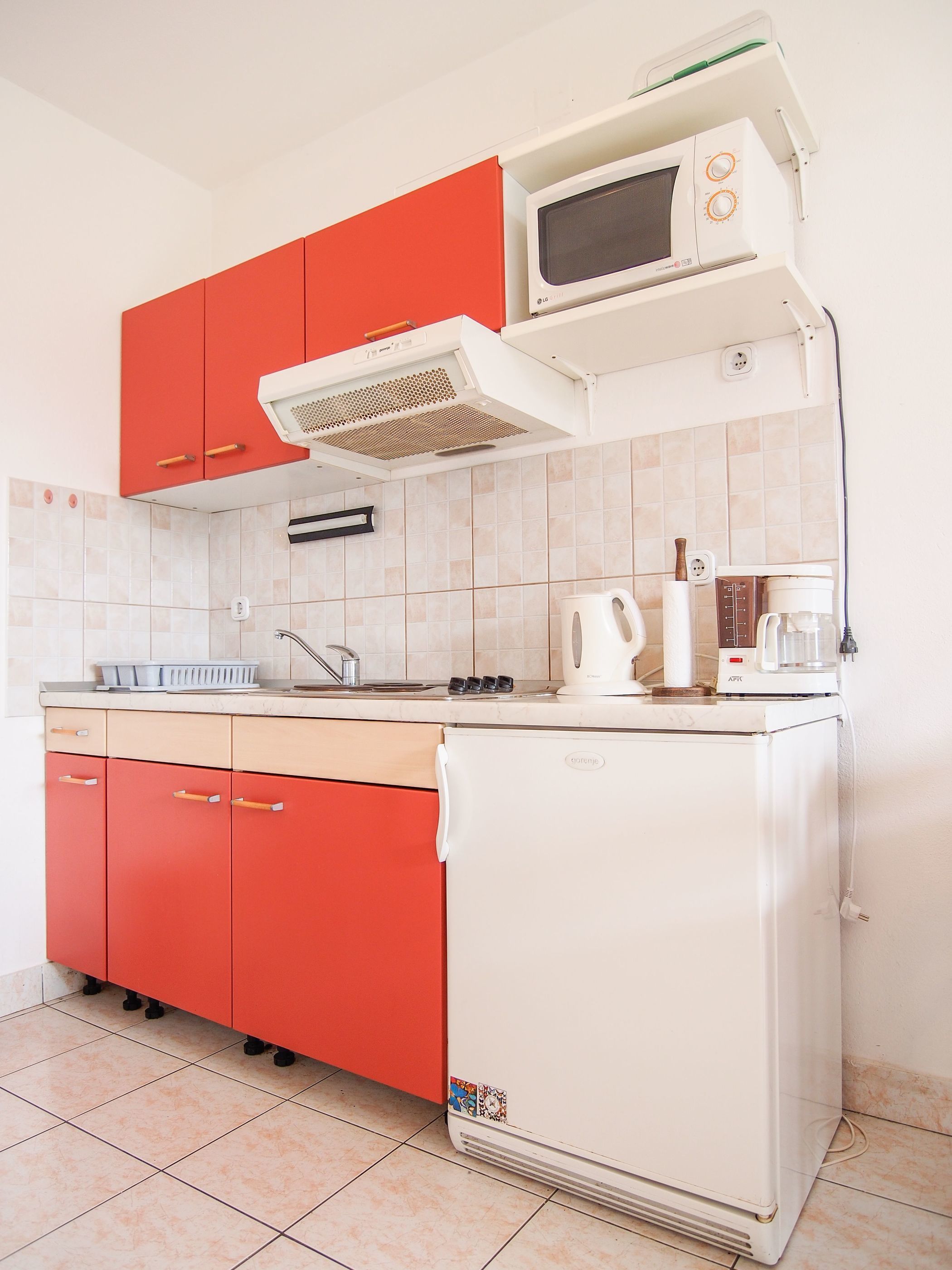 Una cocina compacta con armarios rojos, un refrigerador blanco, un microondas y una cafetera.