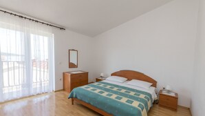 Un dormitorio con cama de madera, mesita de noche, espejo y ventana con cortinas translúcidas.