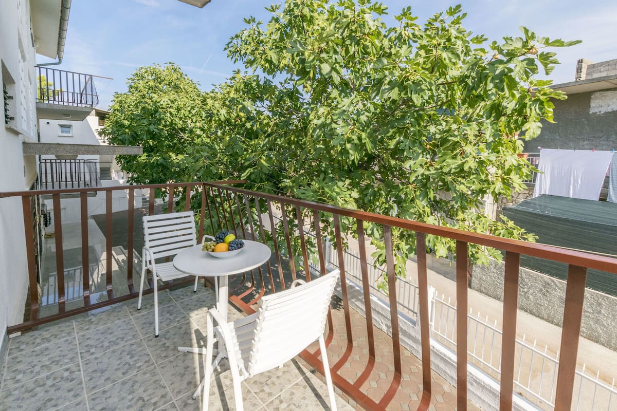 A balcony with a table and chairs, a tree, and a railing.