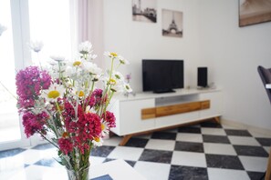Ett vardagsrum med ett rutmönstrat golv, ett vitt TV-bord och en vas med blommor.